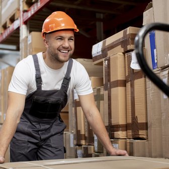 Der Mann mit dem orangefarbenen Helm wirkt zufrieden, während er in einem Lager mit vielen Kartons arbeitet.