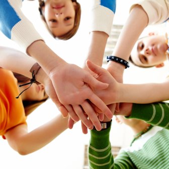 Fünf Hände von Kindern liegen übereinander, symbolisieren Teamarbeit und Freundschaft in einem hellen Raum.