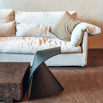 In einem modernen Raum steht ein helles Sofa mit einem Kissen, daneben ein schwarzer Tisch mit einer einzigartigen Form.