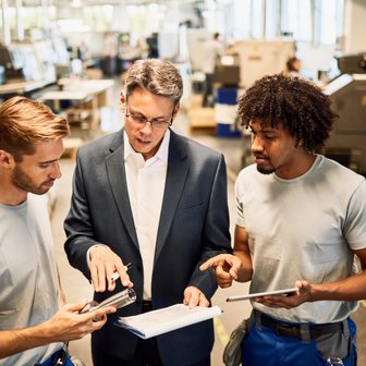 Ein Team von drei Fachleuten analysiert gemeinsam technische Daten in einer modernen Produktionsumgebung.