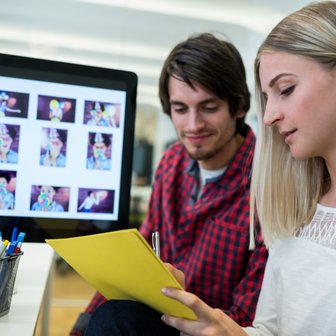 Ein Mann und eine Frau sitzen an einem Tisch, während sie auf einen Computerbildschirm mit bunten Bildern schauen.