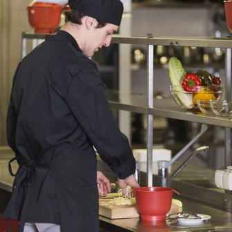 In einer professionellen Küche bereitet ein junger Koch mit einem roten Behälter frische Zutaten vor.