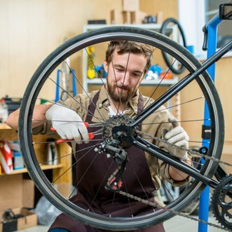 In einer gut ausgestatteten Werkstatt repariert ein Mann ein Fahrrad, wobei er präzise an der Kette und den Speichen arbeitet.