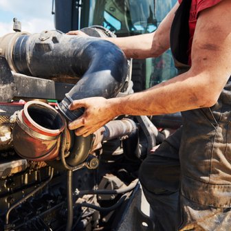 Der Mechaniker konzentriert sich auf die Reparatur eines Traktors, während er ein schwarzes Rohr an die Motorverbindung anbringt.