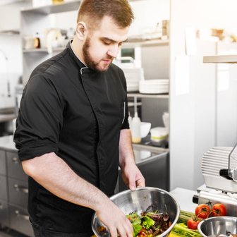 Ein Koch in einer modernen Küche bereitet mit frischen Zutaten einen bunten Salat in einer großen Schüssel vor.