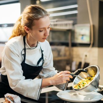Eine Köchin in einer modernen Küche platziert sorgfältig eine bunte Gemüsemischung auf einem weißen Teller.
