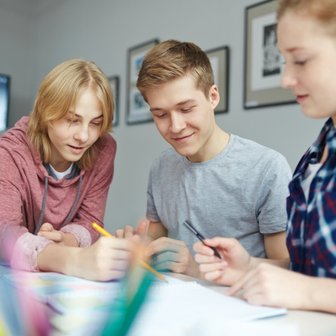 Drei Jugendliche arbeiten gemeinsam an einem Projekt, während sie Notizen machen und sich angeregt unterhalten.