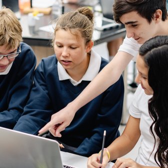 Vier Schüler sitzen um einen Laptop und diskutieren angeregt über den Bildschirm, während einer auf den Bildschirm zeigt.