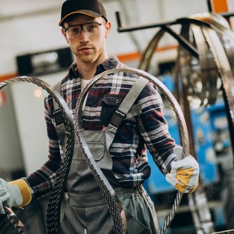 Ein Handwerker in einer Fabrik präsentiert zwei große, glänzende Ringe, während er konzentriert in die Kamera schaut.