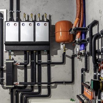 Eine Wand mit verschiedenen Rohren und Ventilen, darunter ein orangefarbener Ausdehnungsbehälter und mehrere Druckanzeigen.