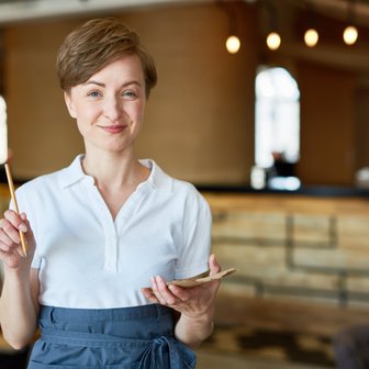 Die freundliche Bedienung trägt ein weißes Hemd und eine blaue Schürze, während sie in einem stilvollen Restaurant steht.