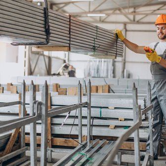 Ein Arbeiter in einem Lagerhaus hebt eine Metallstange an, während er ein mobiles Gerät in der Hand hält und lächelt.