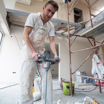 Der Handwerker, bekleidet mit einem fleckigen Overall, konzentriert sich auf das Mischen von Farbe in einem frisch renovierten Raum.