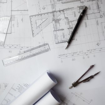 Bauzeichnungen und technische Instrumente wie ein Zirkel und ein Geodreieck sind auf einem Tisch angeordnet, bereit für die Planung.
