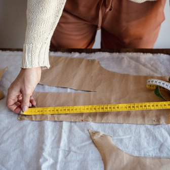 Eine Person misst mit einem gelben Maßband auf einem Tisch, um Schnittmuster aus braunem Papier zu erstellen.