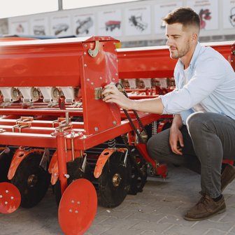 In einem landwirtschaftlichen Umfeld justiert ein Mann eine rote Sämaschine, um sicherzustellen, dass sie einwandfrei funktioniert.