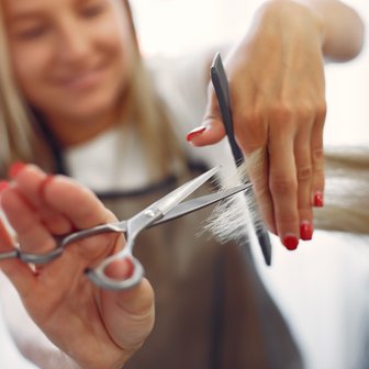 Eine Friseurin schneidet mit einer Schere sorgfältig die Haare, während sie lächelt und konzentriert ist.