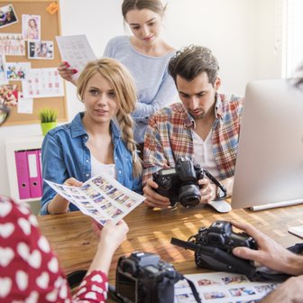 Eine Gruppe von vier Personen diskutiert über Fotos und Kameras an einem Tisch in einem hellen, kreativen Raum.