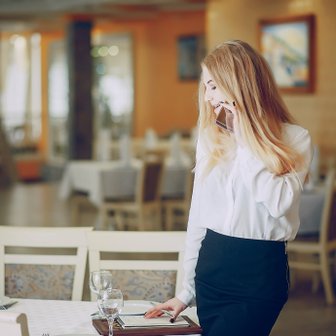 Eine blonde Kellnerin in einem eleganten Restaurant spricht am Telefon, während sie Notizen auf einem Tablet macht.