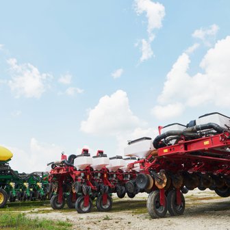 Eine Reihe von landwirtschaftlichen Maschinen steht auf einem Feld unter einem klaren Himmel mit einigen Wolken.