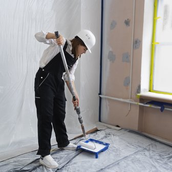 In einem hellen Raum bereitet sich eine Frau darauf vor, die Wand mit einer Farbrolle zu streichen, während sie konzentriert arbeitet.