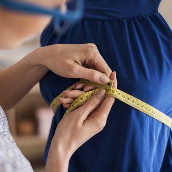 Das Maßband wird um die Taille eines blauen Kleides gelegt, während eine Person präzise Messungen vornimmt, um Anpassungen vorzunehmen.