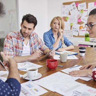 Eine Gruppe von vier Personen diskutiert angeregt über Diagramme und Notizen an einem Holztisch in einem modernen Büro.
