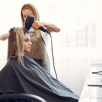In einem modernen Friseursalon wird das Haar einer Frau mit einem Föhn gestylt, umgeben von verschiedenen Haarpflegeprodukten.